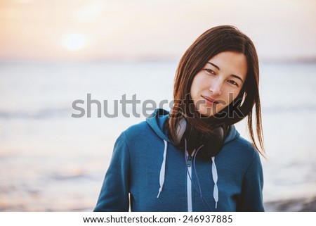 Portrait of beautiful young woman with headphones on background of sea at sunset