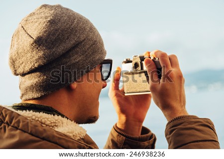 Traveler hipster young man takes photographs with vintage photo camera on coastline near the sea