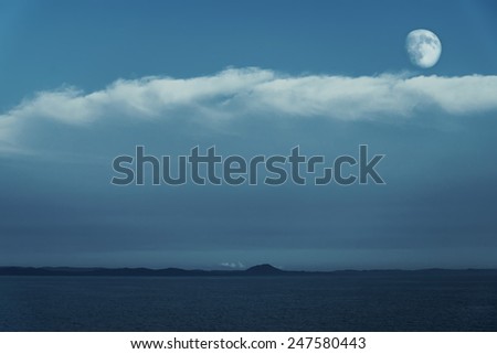 Full moon in blue cloudy sky over the sea
