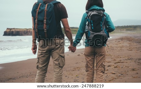 Traveler couple in love with backpacks walking on sea beach in summer and holding each other hand