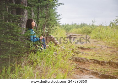 Hiker young woman with backpack resting near the tree in summer forest