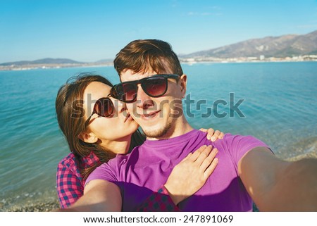 Happy young couple in love taking self-portrait on background of blue sea and woman kissing a man
