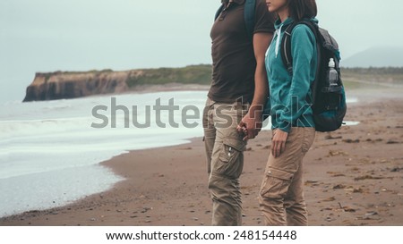 Traveler couple in love with backpacks walking on coastline near the sea in summer and holding each other hand