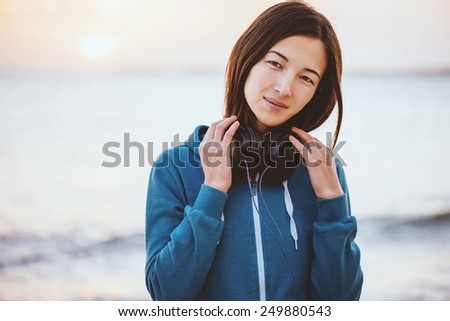 Beautiful young woman with headphones walking on coast near the sea at sunset