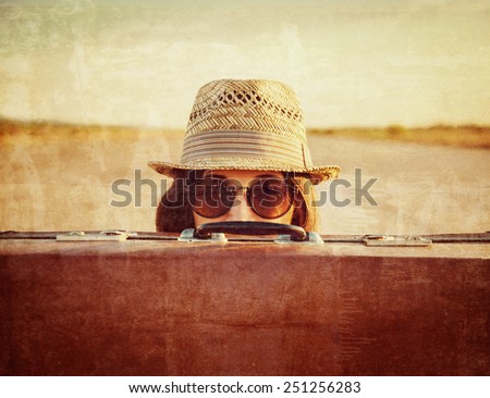 Hipster woman in hat and glasses looks out from vintage suitcase. Vintage image