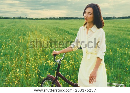 Beautiful young woman resting with a bicycle on summer wildflower meadow