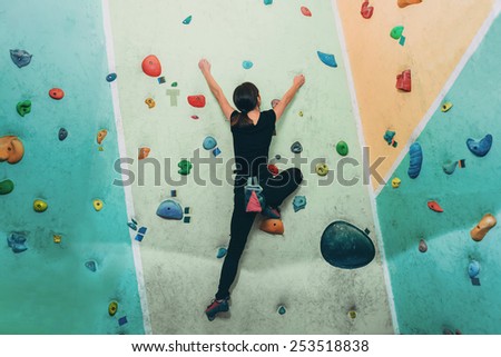 Young sporty woman climbing up on practice rock wall in gym, rear view