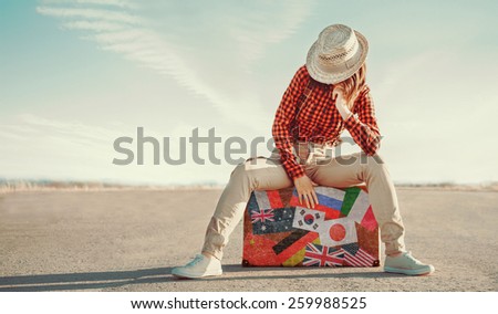 Traveler young woman sitting on a  suitcase on road. Suitcase with stamps flags of different country