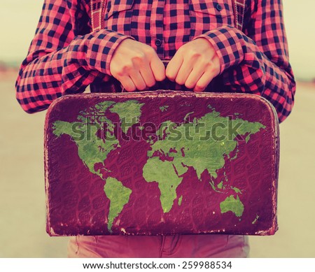 Traveler young woman holding a small suitcase. Suitcase with stamps flags of different country