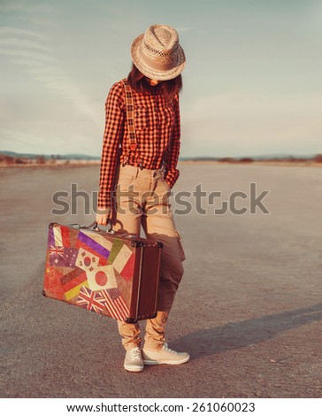 Traveler young woman with a suitcase standing on road. Suitcase with stamps flags of different country
