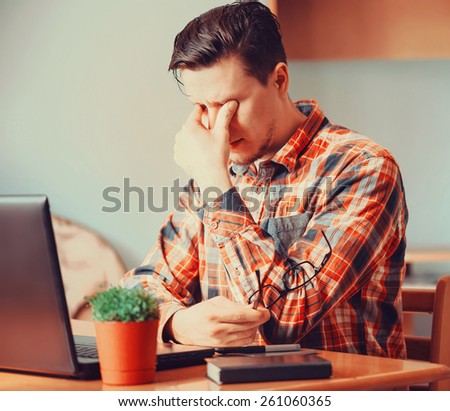 Tired young man sitting over laptop in the office and rubbing his eyes