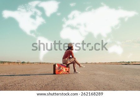 Traveler woman sitting on a suitcase and dreaming about adventures. Map of the world is painted in sky. Concept of travel
