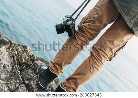 Traveler woman with old photo camera standing on stone coast near the sea. View of legs