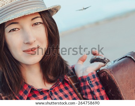 Portrait of smiling traveler young woman with suitcase. Airplane flying in the sky. Concept of travel
