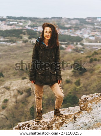 Beautiful young woman dressed in parka and cargo pants standing on hill outdoor
