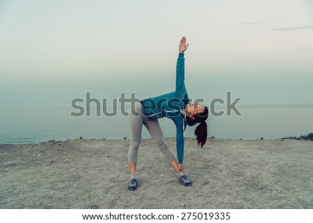 Young woman stretching and preparing to run on coastline in summer in the morning. Concept of sport and healthy lifestyle