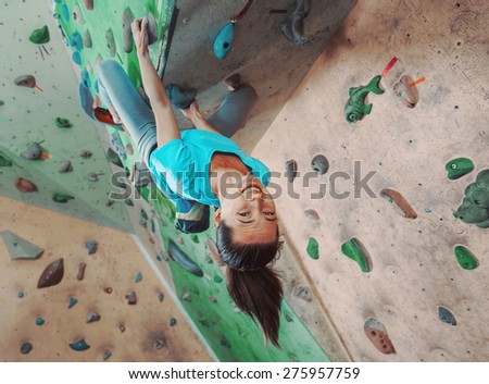 Happy young woman climbing on practical wall indoor, bouldering