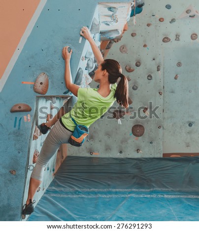Beautiful young woman starts to climbing on practical wall indoor, bouldering