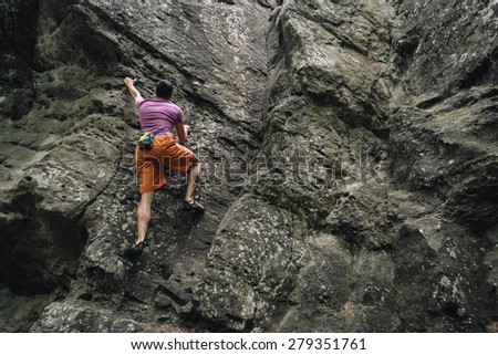 Active young man climbing on stone rock outdoor in summer
