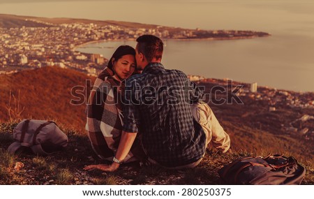 Couple in love sitting on peak of mountain above the town around bay at sunset in summer