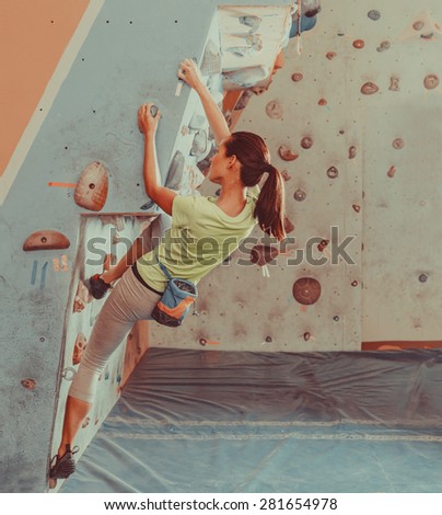 Beautiful young woman starts to climbing on practical wall indoor, bouldering