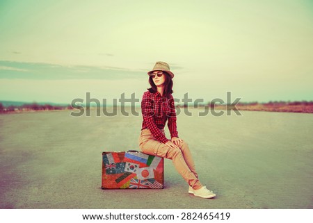 Traveler young woman sitting on a suitcase on road outdoor. Suitcase with stamps flags representing each country traveled