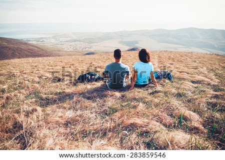 Loving couple sitting on mountain meadow and enjoying view of nature. Image with color effect