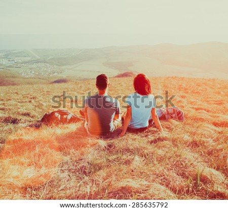 Couple in love sitting on mountain meadow and enjoying view of nature at sunny day in summer