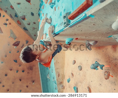 Free climber boy climbing on artificial boulders in gym
