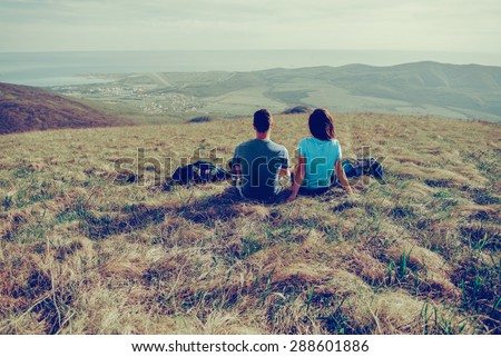 Couple in love sitting on mountain meadow and enjoying view of nature