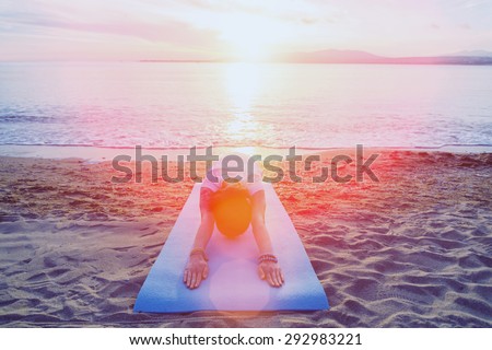 Young woman doing yoga exercise on sand beach near the sea in summer in the morning, woman stretching her back