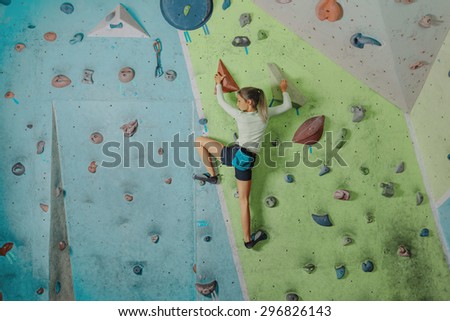 Climber little girl exercises on artificial boulders wall in gym