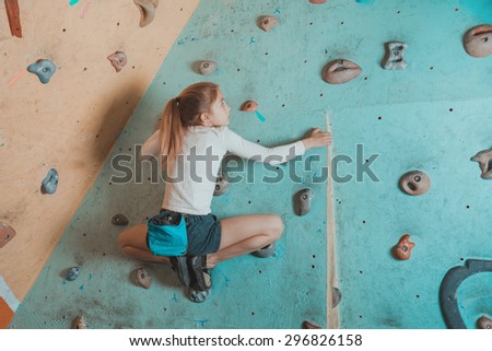 Climber little girl exercises in gym. Climber girl sitting on artificial boulders in pose of frog