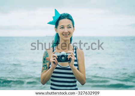Beautiful young woman in costume of sailor standing with old photo camera on background of sea in summer