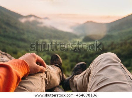 Male traveler sitting in summer mountains at sunset, point of view shot