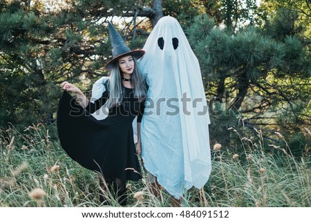 Couple wearing in costume witch and ghost standing in autumn forest outdoor. Theme of Halloween