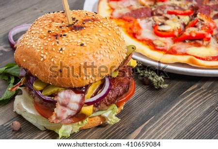 bacon cheese burger with beef patty tomato onion and pizza on a wooden table
