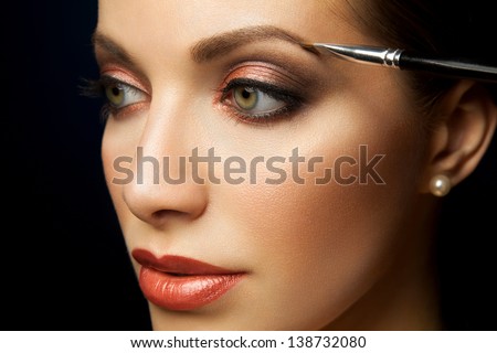 Close-up portrait of a young girl with clean skin with a brush coloring eyebrows on an isolated black background
