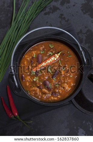 Spicy Mexican soup with red beans and hot chili peppers in a cast iron pot on a wooden table