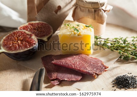Still life composition of cheese, meat, fig, pate and kraft paper packaging on the village boards