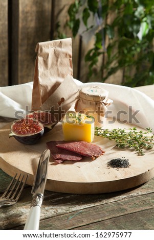 Still life composition of cheese, meat, fig, and kraft paper packaging pate on the village boards