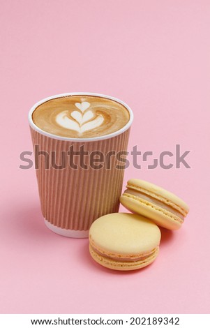 Brown cardboard cup of coffee, cappuccino, with two yellow French macaron cookies on a yellow background