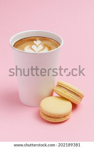 White cardboard cup of coffee, cappuccino, with two yellow French macaron cookies on a yellow background