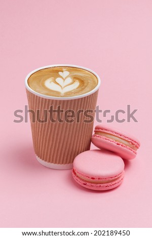 Brown cardboard cup of coffee, cappuccino, with two pink French macaron cookies on a pink background
