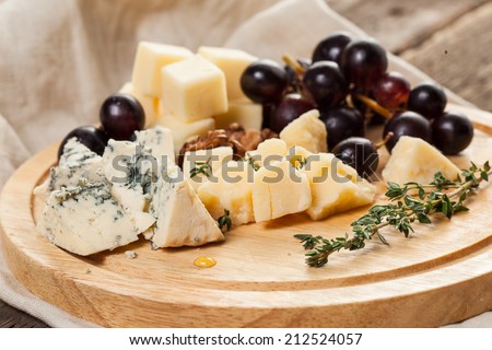 Cheese plate with cheeses Dorblu, Parmesan, Brie, Camembert and Roquefort in serving on the table from an old tree close-up