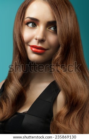 Beautiful girl with long shiny healthy hair on a blue background. Curly brown hair. Red lipstick