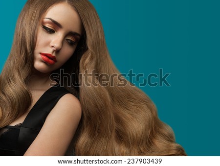 Beautiful girl with long thick shiny hair on a blue background. Curly brown hair. Red lipstick