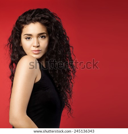 Cute young woman with dark curly hair and perfect skin on a red background