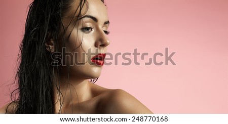 Portrait models with wet skin and long wet hair. Beautiful girl with bronze skin and red lips. Brunette with blue eyes on a pink background.