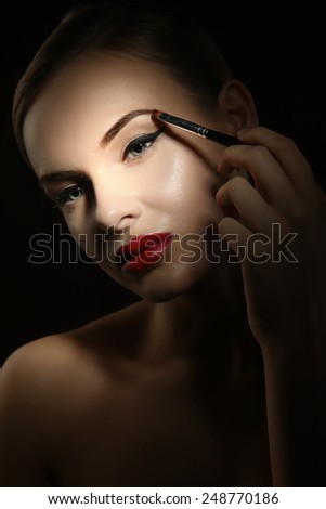 Beautiful woman with perfect skin color eyebrow brush . Blonde with blue eyes and red lips on a black background.